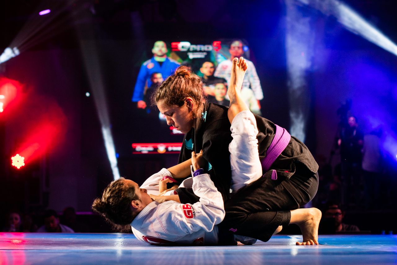 Two women grappling in a jiu-jitsu competition under stage lights