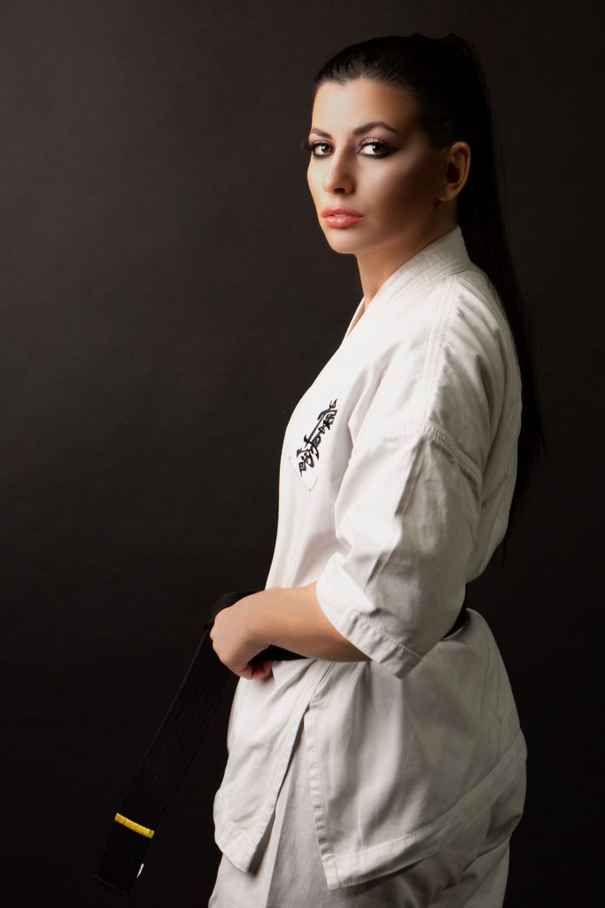 Woman in a white gi holding her belt, photographed against a dark background