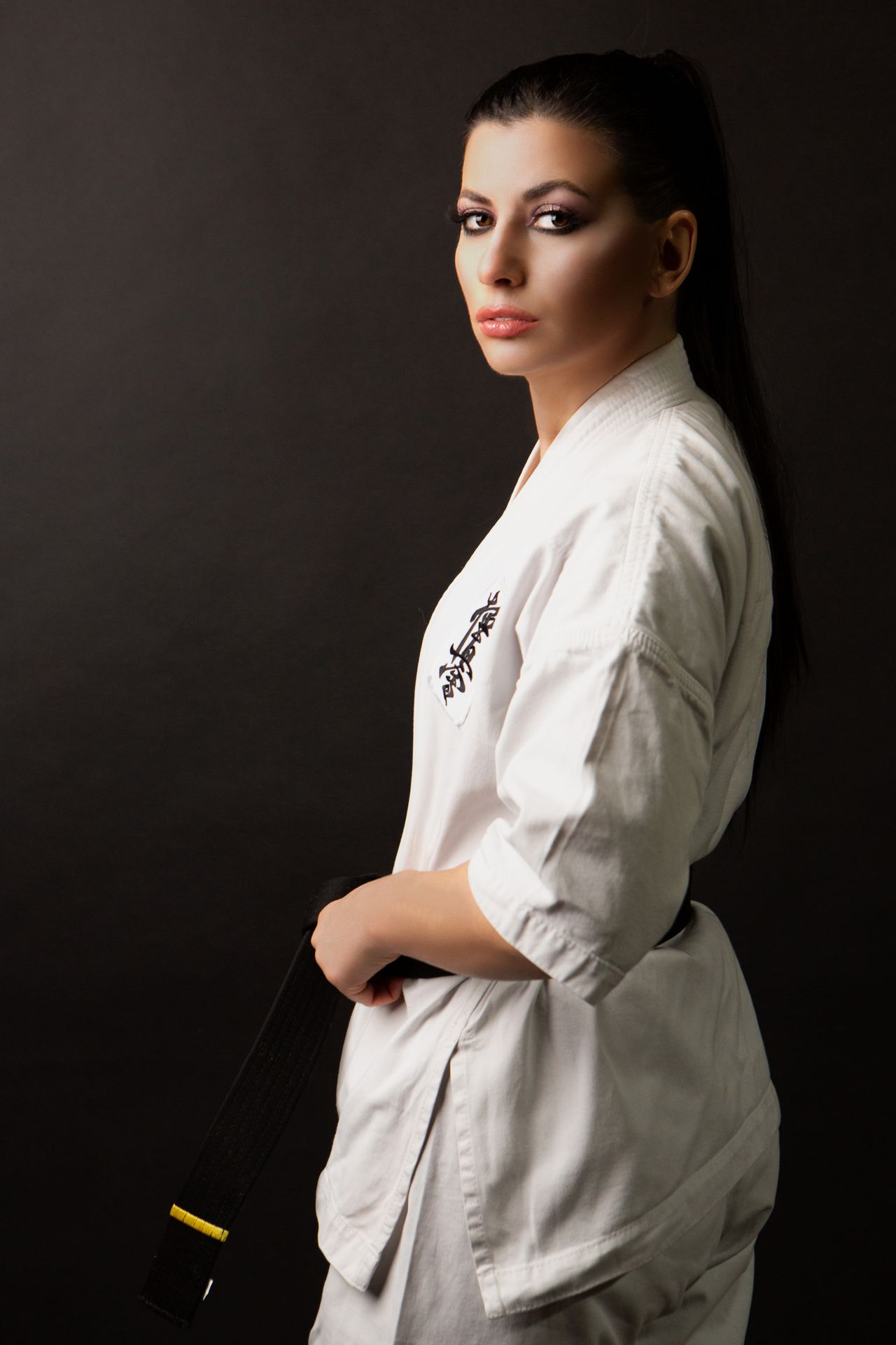 Woman in a white gi holding her belt, photographed against a dark background